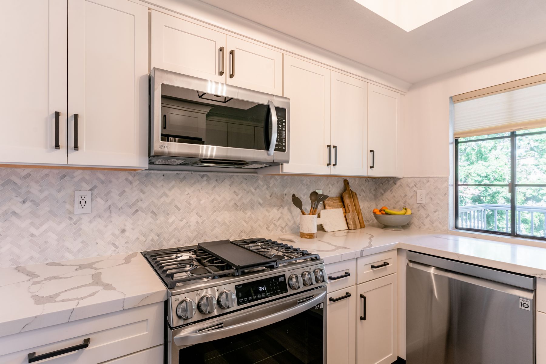 Del Mar condo kitchen with white shaker cabinets, a marble herringbone backsplash and stainless appliances