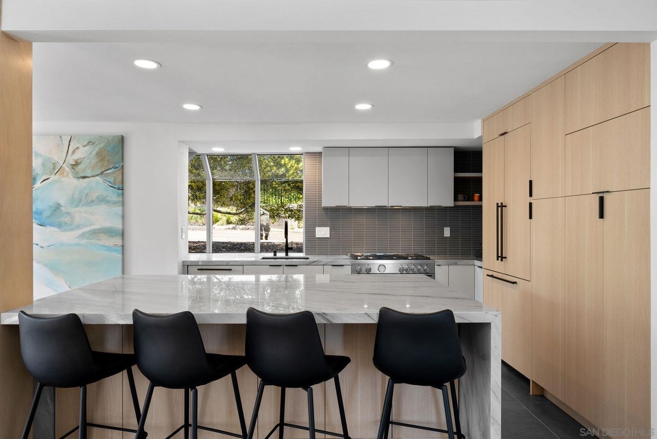 Modern Hillcrest kitchen with a long stone island, black counter stools and light wood cabinetry