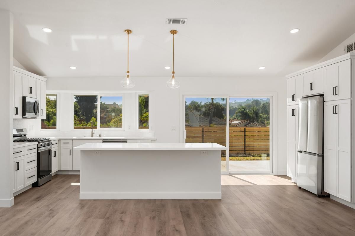 Bright white Oceanside kitchen with a center island, gold pendant lights and wood-look floors