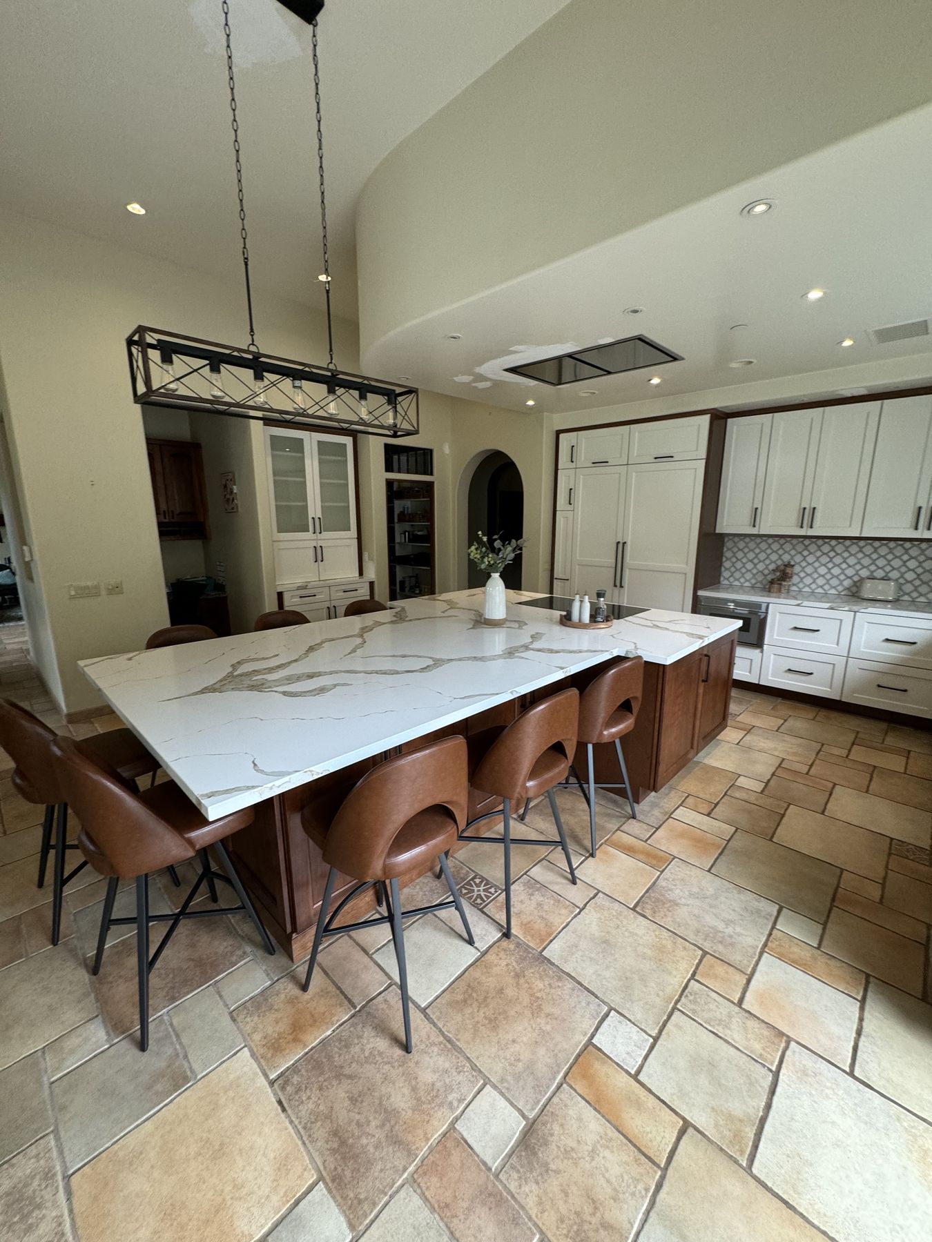 Poway kitchen remodel with a large veined-quartz island, leather counter chairs and a black linear chandelier