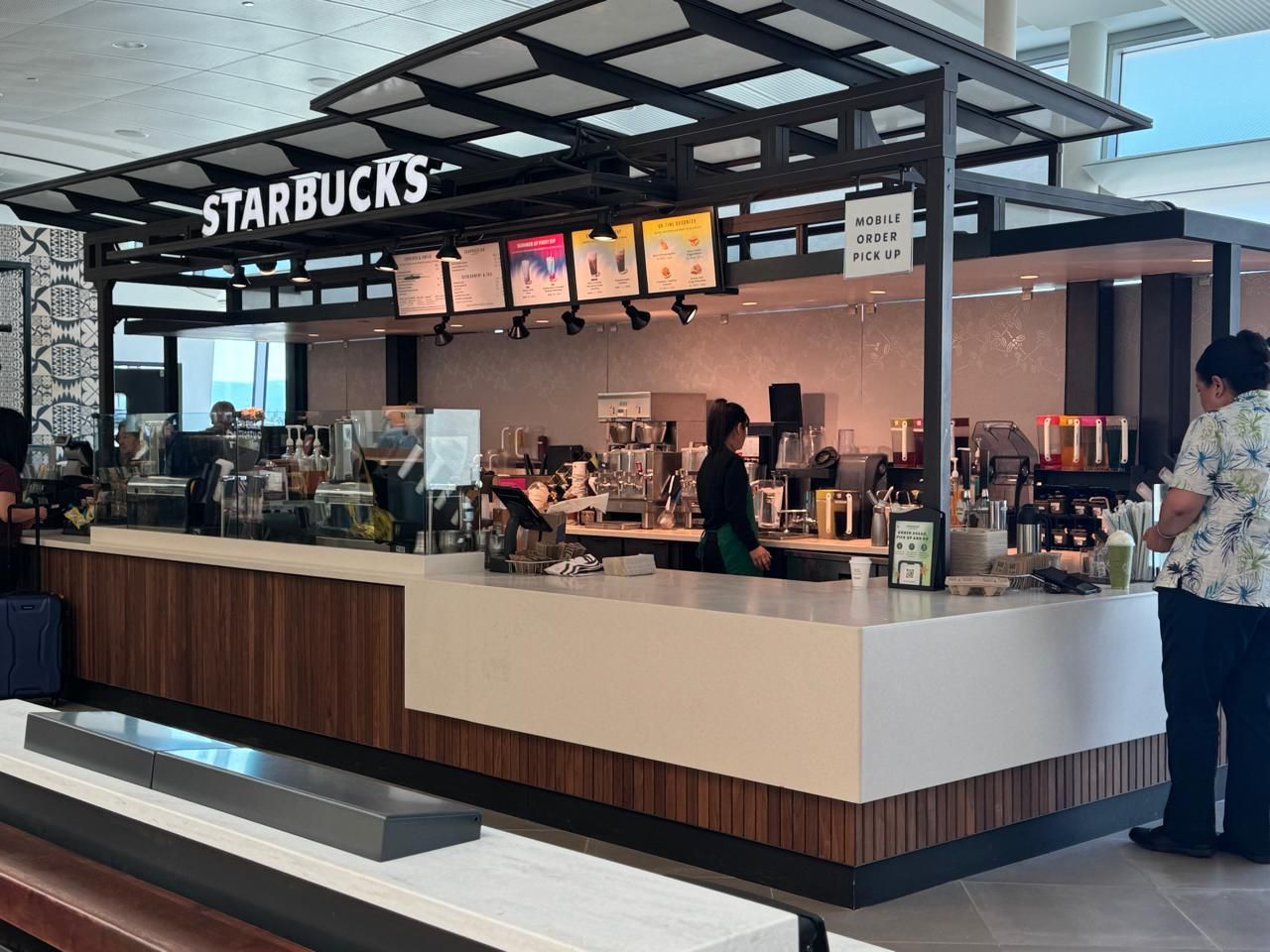 Starbucks kiosk with a steel canopy and wood-slat counter in Terminal B at San José airport